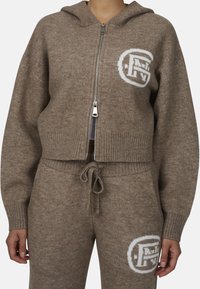 Brązowa, zapinana na zamek, krótka bluza z dzianiny, z białym logo na lewej piersi i ściągaczami na rękawach. W zestawie z dopasowanymi joggerami.