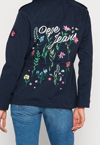 Granatowa kurtka z kolorowym haftem kwiatowym na plecach oraz napisem "Pepe Jeans", wykonana z teksturowanej tkaniny o dopasowanym kroju.