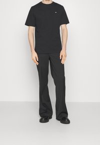 Černé tričko s kulatým výstřihem a malým logem; spárované s černými kalhotami širokého střihu a černými botami, všechno v jednoduchém designu.