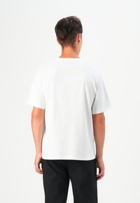 T-shirt en coton blanc à manches courtes, col rond, coupe décontractée et texture lisse, porté avec un pantalon noir. Aucun motif ni accessoire visible.