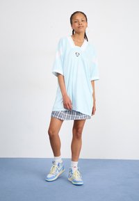 Lys blå oversize trøje med hvide accenter og v-hals. Sammen med en ternet mini-nederdel og lys blå sneakers. Gulvet i baggrunden.