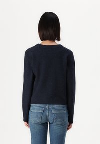 Navy blauwe trui van zacht, textuur stof met een ronde halslijn, lange mouwen en een cropped pasvorm, gecombineerd met lichtblauwe jeans.
