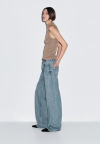 Brun udenærmet top parret med oversized lyseblå jeans. Jeansene har en bred benpasform, bæltestropper og sidelommer.