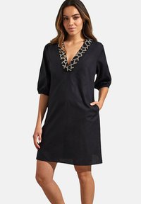 Zwarte linnen jurk met een diepe V-hals en pofmouwen. Bevat een contrasterende geborduurde halslijn en zijzakken. Eenvoudig en modern ontwerp.