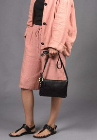 Bolso de mano de cuero negro con textura suave, con detalles en hardware dorado, combinado con un atuendo de lino rosa claro y sandalias negras.