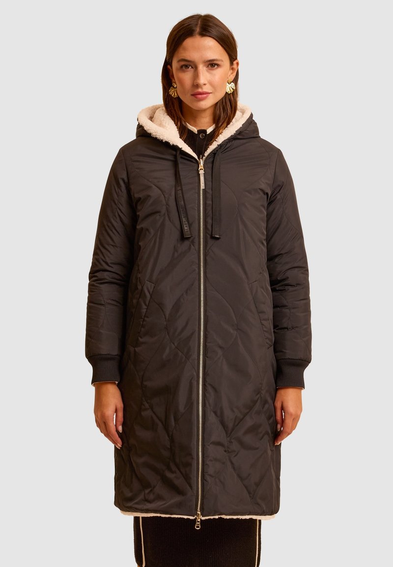 Czarna pikowana parka z zamkiem błyskawicznym, kapturem ze ściągaczem i pluszową, białą podszewką. Posiada ściągacze przy rękawach oraz sięga do kolan.