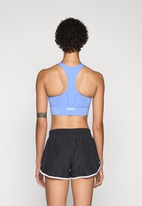 Sports-bh i lyseblått, med racerback-design og teksturert detaljering. Svarte shorts med hvit kant, elastisk liv og synlig logo på siden.