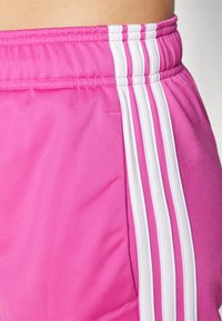 Pink athletic shorts with white side stripes, featuring a textured finish, elastic waistband, and a side pocket.
