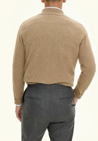Beige gebreide trui met een geribbelde kraag, gedragen over donkergrijze broek. De stof lijkt zacht met een licht fuzzy textuur.