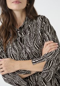 Long-sleeve shirt in dark brown and white, featuring a wave pattern. Buttoned collar and cuffs with a slight sheen. Smooth fabric texture.