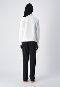 Felpa bianca a collo alto con maniche lunghe, abbinata a pantaloni neri larghi. Texture morbida con una vestibilità comoda, adatta per un abbigliamento informale.