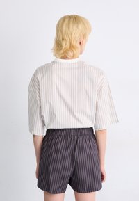 Camicia a maniche corte a righe beige e grigie, abbinata a pantaloni corti grigi a righe. Vestibilità ampia, con cintura elastica sui pantaloni.
