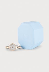 Montre en argent et or rose avec un cadran gris clair texturé et des accents en diamant, accompagnée d'une boîte octogonale bleu clair.