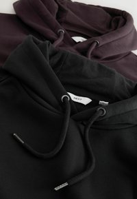Zwei Hoodies, einer schwarz und einer dunkelviolett, aus weichem Stoff. Der schwarze Hoodie hat runde Kordelzugöffnungen und metallicfarbene Enden.