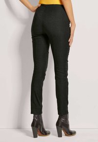 Schwarze, taillierte Hose von hinten, mit hoher Taille und schmal zulaufenden Beinen, kombiniert mit schwarzen, heeled Knöchelboots. Glatte Stofftextur.