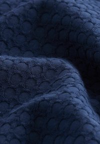 Marineblauwe textuurstof met een bubbeltjespatroon, met een zachte, verweven structuur. Het oppervlak heeft een lichte glans en diepte.