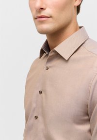 Camicia button-up marrone chiaro con una trama testurizzata, caratterizzata da un colletto interno a fantasia e bottoni marroni a contrasto.