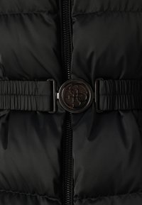 Gilet imbottito nero con chiusura frontale a zip, vita cinchata con una cintura a coste e una fibbia in metallo rotonda con un design intricato.