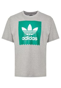Grå bomullströja med en grön rektangulär grafik som har vit text "adidas" och en klassisk trefoil-logotyp i mitten.