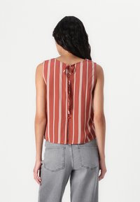 Rødstribet ærmeløs top med en rygsløjfe og et cropped design, lavet af et glat stof. Sammen med lysegrå jeans.