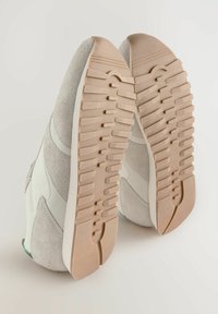Weiße und graue Sneakers aus Wildleder und Leder; strukturierte Gummisohlen mit horizontalen Rillen; abgerundete Zehenpartie und minimalistisches Design.