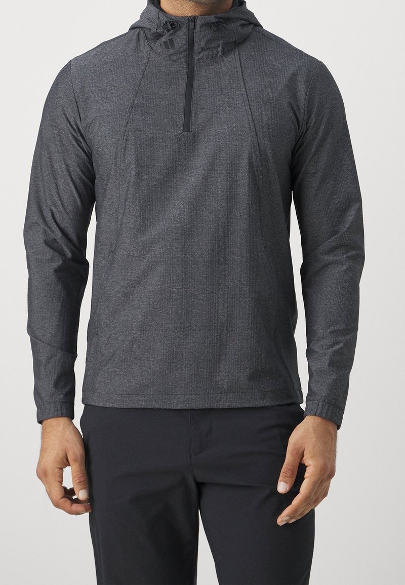 Tmavě šedý lehký pulovr s čtvrtinovým zipem, kapucí a dlouhými rukávy. Má strukturovanou látku a elastické manžety pro těsné přilnutí.