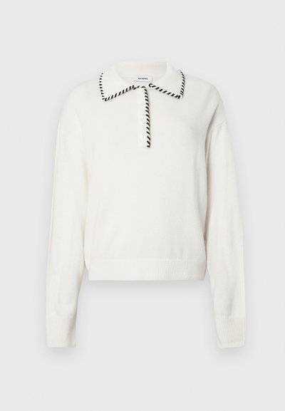Hvitt strikket gensere med svart trim rundt kragen, og knapper foran samt ribbestrikkede mansjetter og nederkant for en tettsittende look.