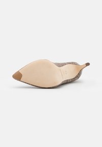 Zapato de tacón alto con punta afilada que presenta un upper texturizado en marrón con un acabado brillante y una suela beis, destacando una silueta elegante.