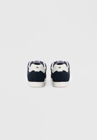 Tenisky s horní částí z tmavě modrého semiše s bílými detaily, zaobleným tvarem a bílou gumovou podrážkou. Zadní značka je viditelná nad patou.