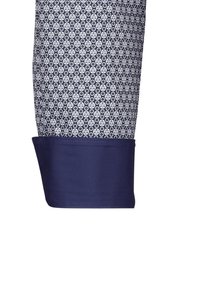 Camicia blu navy con un tessuto a motivo caratterizzato da piccole cerchie bianche. Il polsino ha un bordo blu navy uniforme, evidenziando toni a contrasto.