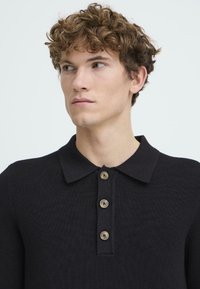 Mustat polo-paitat, joissa on teksturoitu kangas, klassinen kaulus ja neljä ruskeaa napin suljinta läpän kohdalla.