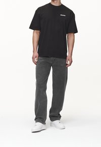 Camiseta negra con cuello redondo y mangas cortas, combinada con jeans gris oscuro y zapatillas blancas, con un pequeño gráfico en el pecho.