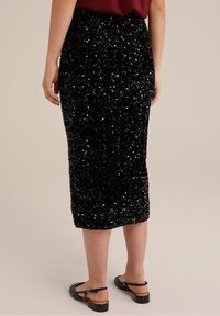 Svart, paljettbeströdd midijurk med en figurnära silhuett, som har en texturerad yta och ett elastiskt midjeband, kombinerad med svarta platta sandaler.