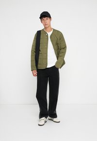 Alyvuogių spalvos siuvinėtas švarkas su spaudėmis, užsidėtas ant baltos marškinės ir derinamas su juodomis kelnėmis. Papuoštas juodu kepurėle ir krepšiu.