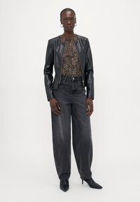 Black leather jacket, patterned brown top, high-waisted gray jeans, and black pointed heels. Model stands against a light background.