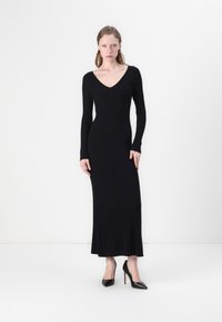 Black ribbed long-sleeve dress with a V-neckline and fitted silhouette, featuring a flared skirt. Paired with black pointed-toe heels.