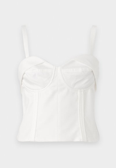 Bela skrajšana braletta z nastavljivimi naramnicami, mehko tkanino, strukturiranim korzetom, ukrivljenim izrezom in stranskimi šivi za definicijo.