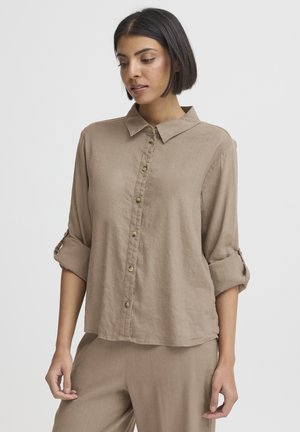 Chemise en lin marron avec col, boutonnage devant et manches retroussées. Présente une coupe décontractée et une texture douce, complétée par des boutons en laiton.