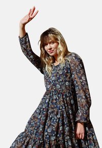 Abito floreale a maniche lunghe con una base scura e un mix di motivi blu, arancione e bianchi. Gonna a campana e elementi di design a strati.