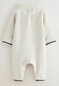 Bodysuit pour bébé à manches longues en crème clair avec un motif texturé, présentant une patte de boutonnage au niveau du cou et des poignets rayés.