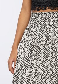 Gonna a smock bianca e nera con motivo a foglie, realizzata in tessuto leggero e design plissettato, con vita elasticizzata per il massimo comfort.