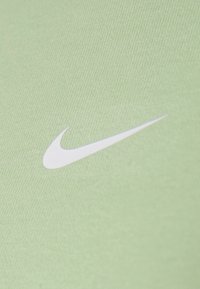 Tejido atlético verde con el logo de Nike Swoosh en blanco. La textura es suave y presenta un patrón de punto fino.