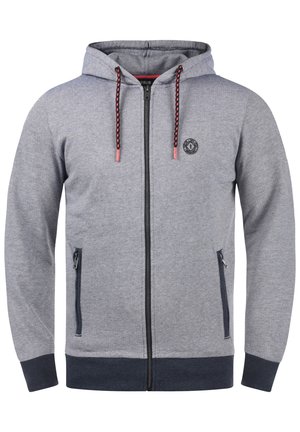 Harmaa vetoketjullinen huppari, joka on valmistettu teksturoidusta kankaasta. Hupparissa on huppu, kaksinkertaiset sivutaskut, mustat yksityiskohdat ja kuviolliset narut. Pyöreä logo rinnassa.