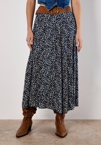 Flared, ankle-length skirt in navy blue with white abstract pattern, made from lightweight fabric, paired with a woven brown belt and brown boots.