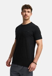 Sort kortærmet t-shirt lavet af blødt bomuld. Har en brystlomme og en rund halsudskæring, vist på en mandlig model.