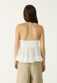 Top bianco senza maniche con corpetto arricciato e orlo a balze, realizzato in tessuto leggero. Fascia sul retro per una vestibilità regolabile.