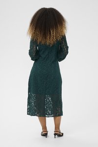 Dark green lace midi dress with long sleeves, floral pattern, textured fabric, and a fitted silhouette. Worn with black ankle-strap heels.