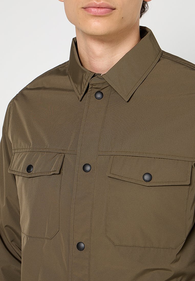 Chemise olive verte à boutons avec col, deux poches poitrine, matériel noir et texture lisse. Présente une coupe décontractée et un design minimal.