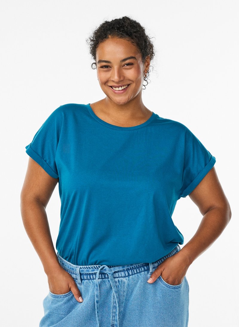 Turquoise short-sleeve t-shirt with a round neckline, made from soft fabric. Loose fit with rolled sleeves, worn with light blue drawstring pants.