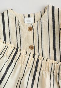 Robe en coton rayée crème et marine, avec un col rond, deux boutons en bois au niveau de l'encolure, et une taille élastiquée.